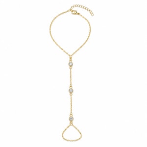 May include: A gold-toned hand chain featuring a delicate cable chain design. The piece includes three round, clear, bezel-set stones spaced evenly along the central vertical chain, connecting a wrist bracelet to a finger loop at the base.