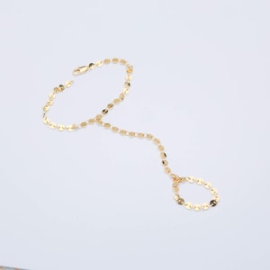 May include: A gold-toned hand chain bracelet featuring a delicate design of small, flat, circular metallic discs linked together. The piece includes a circular ring component connected by a chain segment to a larger wrist bracelet section.
