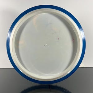 May include: A white and blue disc golf disc with a blue rim. The disc has a white center and a blue outer edge. The text "GYRO" is printed on the blue rim. The disc is designed for disc golf.