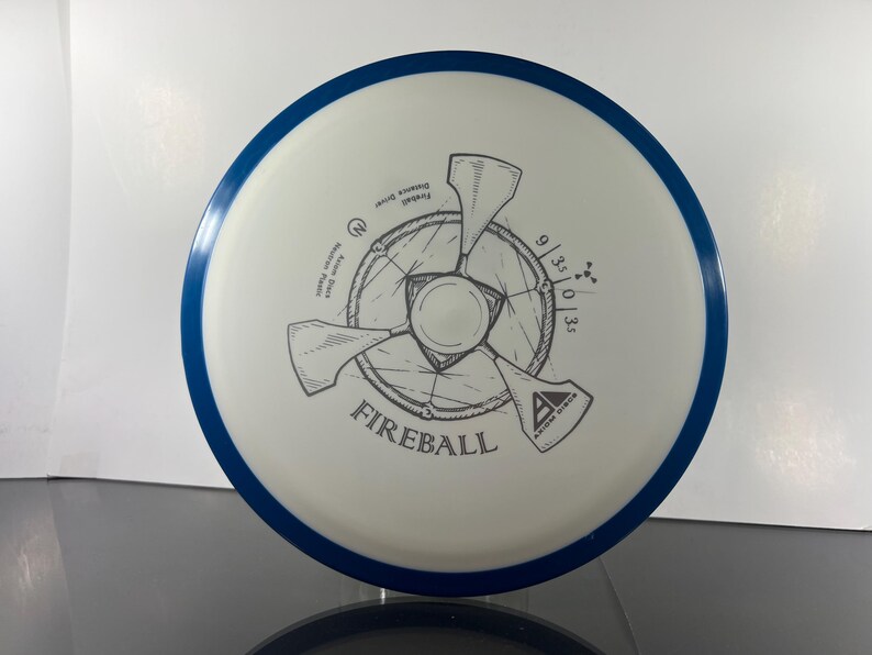 May include: A white disc golf disc with a blue rim. The disc features a gray graphic design of a propeller-like shape with the word "FIREBALL" and the Axiom Discs logo. The disc has the numbers 9/3/0/3.5 printed on it.