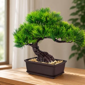 May include: An artificial bonsai tree featuring vibrant green needle-like foliage and a textured dark brown trunk. The tree is planted in a rectangular dark brown plastic pot filled with small, light-colored decorative pebbles at the base.