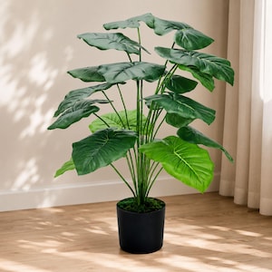 May include: A tall artificial plant with large, broad, heart-shaped green leaves arranged on slender stems. The plant is potted in a simple, solid black cylindrical container, with the base of the stems covered by a layer of dark green moss.