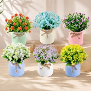 May include: Six small potted artificial plants in various colors. Each plant features vibrant flowers and green foliage housed in a ceramic jar tied with a rustic jute twine bow. The pots come in pastel shades of mint, cream, pink, blue, white, and light blue.