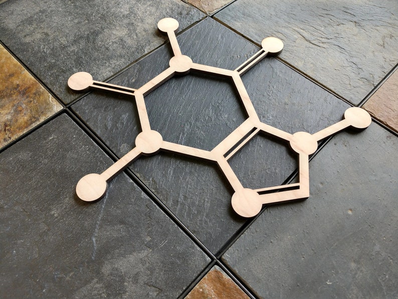 Op de afbeelding: Een houten uitsnijding van een chemische structuur, die lijkt op een hexagon met extra ringen en takken, op een grijs betegeld oppervlak.