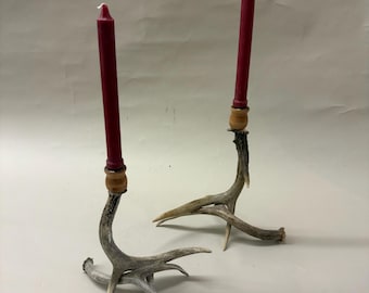 May include: Two rustic candle holders with red candles. The candle holders are made from antlers, with a natural, weathered appearance. The candles are tall and slender, adding a touch of elegance to the rustic design.