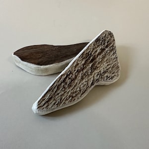 May include: Two pieces of antler, one is a light brown color and the other is a darker brown color. The antler pieces are smooth and have a natural texture.