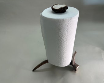 May include: A white paper towel roll holder made from two antler branches. The holder has a brown antler top with a white ceramic disc on top.