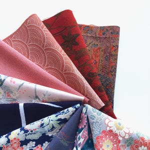 May include: A collection of eight fabric swatches in various shades of red, pink, blue, and gray. The fabrics feature different patterns, including floral, geometric, and abstract designs.