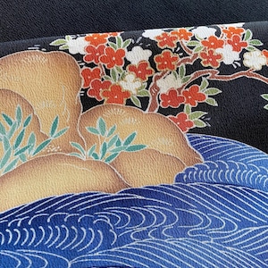 Pode incluir: Close-up de um tecido com um design de inspiração japonesa. O design apresenta rochas marrons com folhagem verde, um padrão de ondas azuis e um fundo preto com flores vermelhas e brancas.