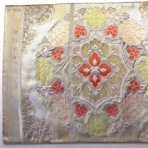 May include: A rectangular textile panel featuring a metallic silver background with intricate embroidery. The design includes repeating floral motifs in shades of coral, pale yellow, and silver, centered around a symmetrical geometric medallion.