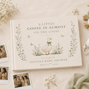 May include: A rectangular guest book with a cream cover featuring a central illustration of a goose wearing a green bow, surrounded by wildflowers and butterflies. The text reads A LITTLE GOOSE IS ALMOST ON THE LOOSE, GUEST BOOK, OLIVIA'S BABY SHOWER, JULY 11TH 2026.
