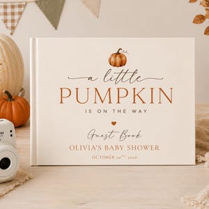 May include: A rectangular guest book with a cream cover featuring a watercolour pumpkin illustration and the text: A little PUMPKIN IS ON THE WAY Guest Book OLIVIA'S BABY SHOWER OCTOBER 10TH, 2026. The design includes a small orange heart.