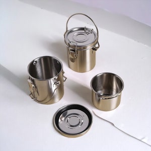 May include: Four silver metal containers with lids and handles. Two of the containers are open, revealing the silver interior. One container has a black rubber seal around the lid.