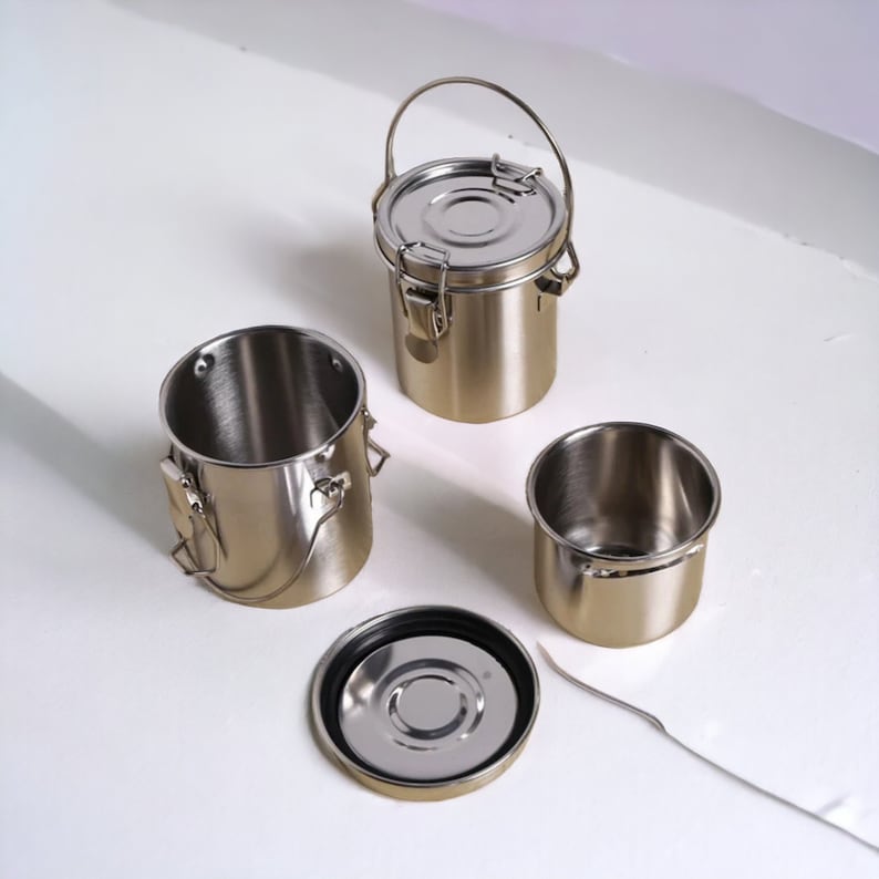 May include: Four silver metal containers with lids and handles. Two of the containers are open, revealing the silver interior. One container has a black rubber seal around the lid.