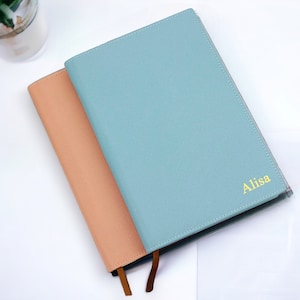 May include: Two notebooks with personalized names. The top notebook is light blue with the name "Alisa" in gold lettering. The bottom notebook is peach.