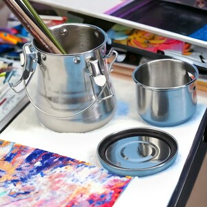 May include: A set of three stainless steel paint brush cleaning containers. The largest container has a lid and a handle. The smallest container is a lid for the medium-sized container.