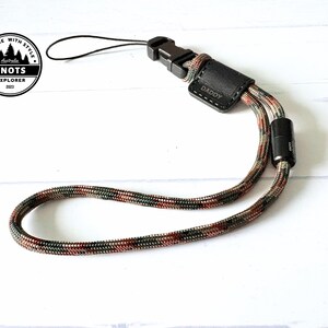 Op de afbeelding: Een polsband met een camouflagepatroon in bruin, groen en rood. Het heeft een zwarte plastic gesp en een klein leren stukje met het woord "DADDY" in reli&euml;f. De band is ontworpen voor het vastzetten van items. Lengte ongeveer 20 cm.