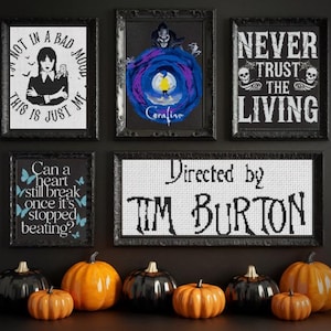 May include: A collection of framed cross-stitch art with gothic and Halloween themes. The art includes quotes, movie references, and images. Orange and black pumpkins are displayed below the framed art.