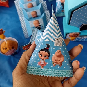 Puede incluir: Un cono de fiesta azul y blanco en forma de cono con un patrón de zigzag. El cono presenta una imagen de dibujos animados de una niña y un niño. El cono tiene un borde festoneado.