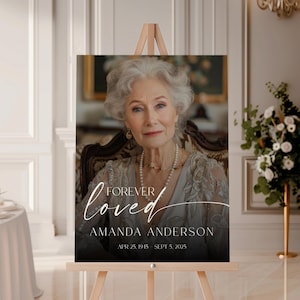 May include: A memorial sign on a wooden easel features a portrait of an older woman with the words "Forever Loved" and the name "Amanda Anderson" along with her birth and passing dates. The portrait is in a formal setting.
