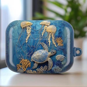 May include: Blue case featuring an underwater scene with jellyfish, a sea turtle, and coral. The case has a textured appearance with detailed relief elements. The design incorporates shades of blue, gold, and white, creating a marine theme.