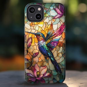 May include: A colorful phone case featuring a stained-glass design with a hummingbird and flowers. The hummingbird has vibrant blue, green, and purple feathers, with pink and orange wings. The background is a mosaic of yellow, orange, and green.