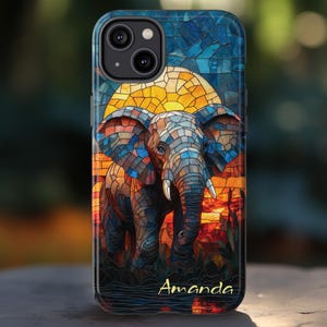 May include: A phone case featuring a stained-glass style elephant design. The elephant is depicted in shades of blue, orange, and brown, set against a sunset backdrop. The name "Amanda" is written in gold script at the bottom.