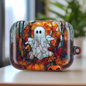 May include: A clear, protective case for earbuds featuring a stained-glass design. The artwork depicts a white ghost, pumpkins, and autumn leaves in shades of orange, red, and brown. The case has a small loop for attaching to a keychain.