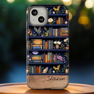 May include: A blue and brown phone case with a bookshelf design featuring books, flowers, and butterflies. The bottom of the case has a woodgrain pattern and the name "Sharon" is written in cursive.