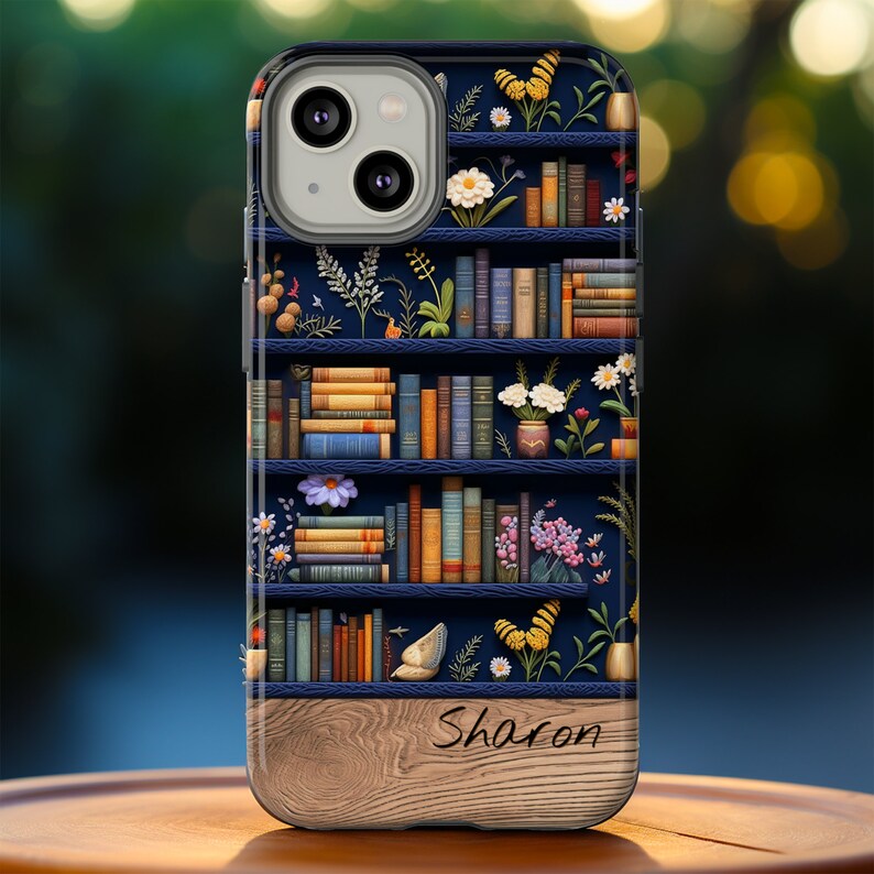 May include: A blue and brown phone case with a bookshelf design featuring books, flowers, and butterflies. The bottom of the case has a woodgrain pattern and the name "Sharon" is written in cursive.