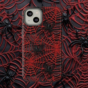 May include: A black phone case with a red spiderweb design. The case features a black spider silhouette in each corner of the web.