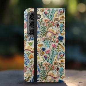 May include: A phone case featuring a colorful floral and book design. The case has a black elastic band and a camera cutout. The design includes various flowers, open books, and leaves in shades of pink, blue, yellow, and green.