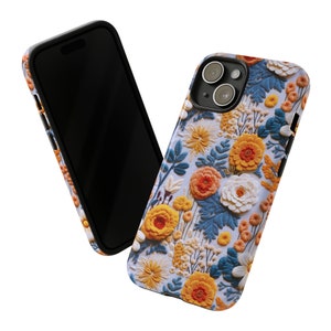 Pode incluir: Uma capa de telefone com um design floral com flores amarelas, laranja e brancas sobre um fundo azul. A capa tem um recorte para a lente da c&acirc;mera.