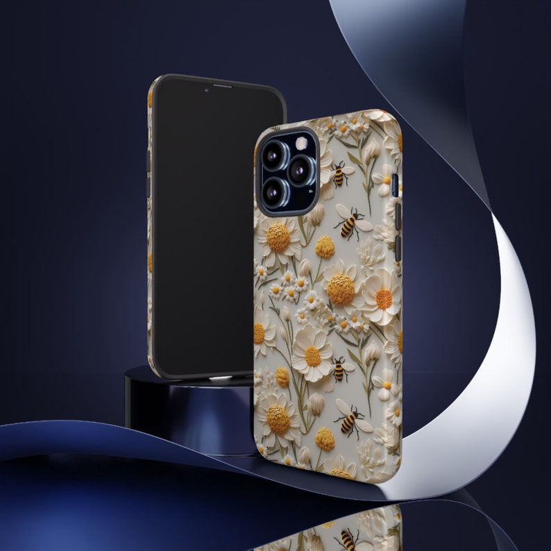 Pu&ograve; includere: Una custodia per telefono bianca con un motivo floreale con margherite gialle e bianche e api. La custodia &egrave; progettata per un iPhone.