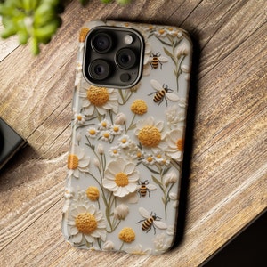 Pu&ograve; includere: Custodia per telefono bianca con un design floreale con margherite bianche e centri gialli. Le api sono sparse in tutto il design.