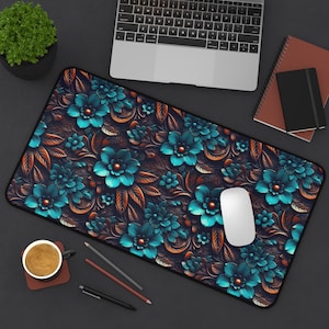 May include: A rectangular desk mat featuring a floral design with teal and orange flowers on a dark background. The mat is surrounded by a black border. A white computer mouse sits on the mat, near a laptop.