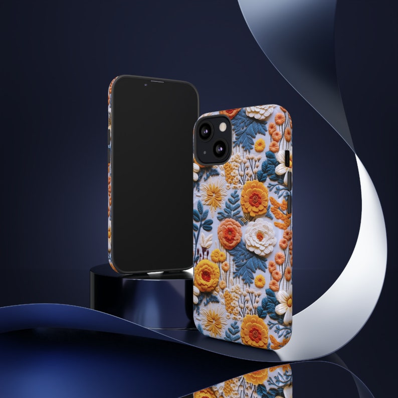 Pode incluir: Uma capa de telefone preta com um design floral. A capa apresenta uma variedade de flores em tons de amarelo, laranja, branco e azul. As flores est&atilde;o dispostas em um padr&atilde;o repetitivo sobre um fundo branco.