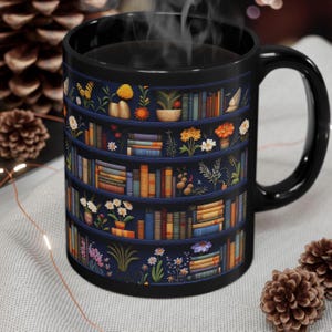 May include: Black coffee mug with a design of a bookshelf filled with books and flowers. The bookshelf is on a dark blue background.
