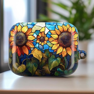 May include: A protective case for earbuds featuring a stained-glass design of sunflowers. The case has a dark blue background with yellow, orange, and blue floral details. The case has a small loop for attaching to a keychain.