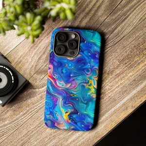 May include: A smartphone case with a vibrant, abstract design. The case features a swirling pattern of blues, purples, yellows, and pinks, creating a colorful, marbled effect. The case has a camera cutout and is set on a wooden surface.
