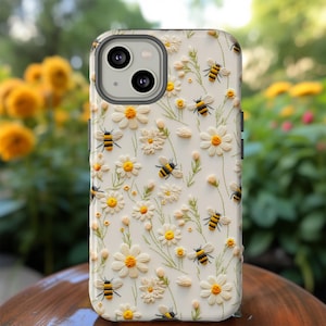 Könnte beinhalten: Eine weiße Handyhülle mit einem Blumen- und Bienenmuster. Die Hülle zeigt gestickte Gänseblümchen und Bienen in Gelb und Schwarz.