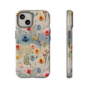 May include: A floral phone case featuring a colorful embroidered design. The case displays a variety of flowers in shades of red, yellow, blue, and pink against a light blue and white background. The case is shown from the front and side.
