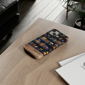 May include: A personalized phone case with a blue and brown design featuring a bookshelf filled with books and flowers. The name "Sharon" is engraved on the wooden side of the case.