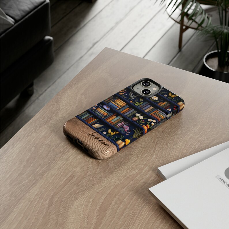 May include: A personalized phone case with a blue and brown design featuring a bookshelf filled with books and flowers. The name "Sharon" is engraved on the wooden side of the case.
