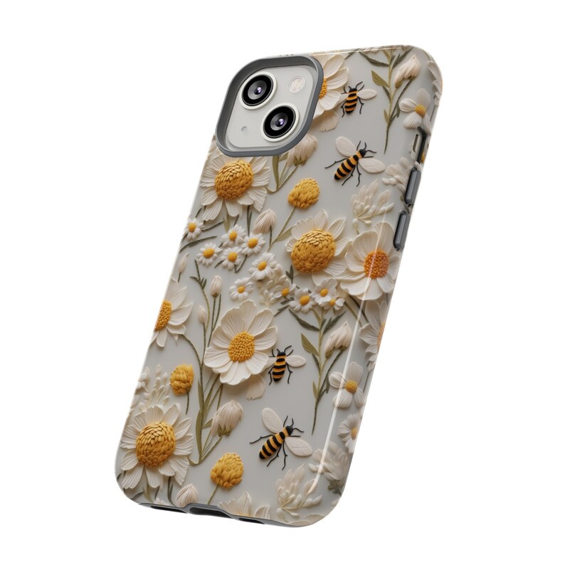 Pu&ograve; includere: Una custodia per telefono bianca con un design floreale con margherite bianche e centri gialli. La custodia presenta anche un motivo di piccole api gialle e nere.