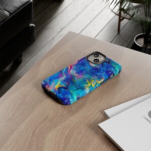 May include: A smartphone case with a vibrant, abstract design. The case features a swirling pattern of blues, greens, yellows, and pinks, creating a colorful, marbled effect. The case is on a light-colored wooden surface.