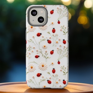 May include: White iPhone case with a floral pattern featuring red ladybugs and white daisies.