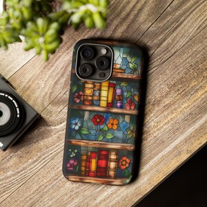May include: A phone case with a stained glass design featuring a bookshelf with colourful books and flowers. The case has a camera lens cutout and a black border.