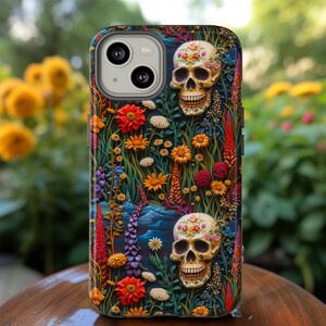 Peut inclure: Une coque de t&eacute;l&eacute;phone avec un motif floral color&eacute; et deux cr&acirc;nes en sucre. Les cr&acirc;nes sont orn&eacute;s de fleurs et sourient. L'arri&egrave;re-plan est bleu fonc&eacute; avec une touche de vert.