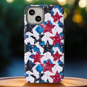 May include: A smartphone case with a patriotic star pattern. The case features a white background with a repeating design of red, blue, and black stars. The stars have a textured, painted appearance, and the case has a glossy finish.